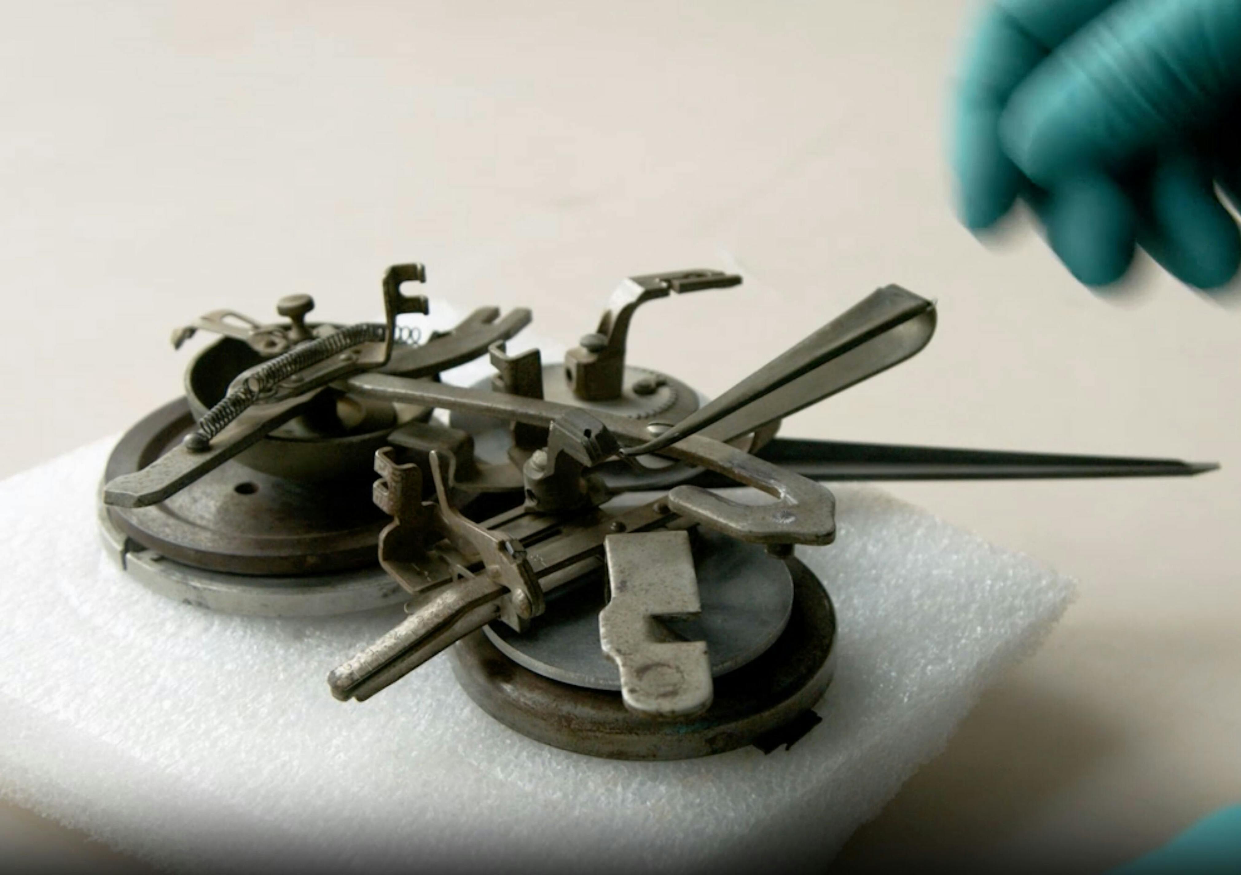 A small metal sculpture made up of two round disks with various metallic pieces of different shapes on top, sits on a flat white surface.